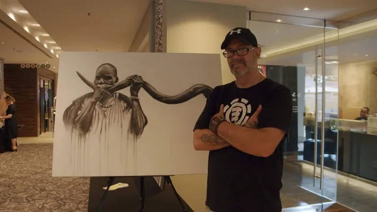 Ian Maree standing beside a painting at an exhibition