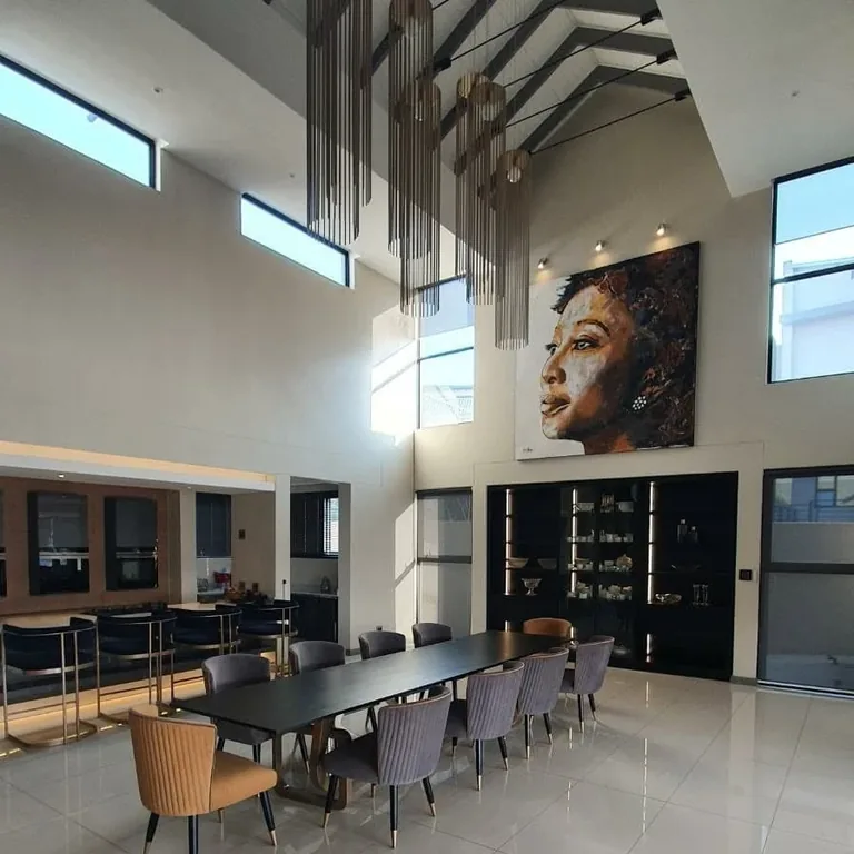 A large portrait painting displayed above a dining area in a light-filled interior